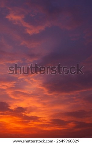 This image beautifully captures a sunset sky filled with vibrant and warm tones. The scene transitions from golden orange and fiery red near the horizon to deep purples and indigos at the top.