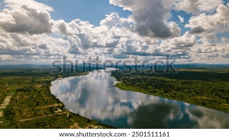 This image beautifully captures the Volta River in Ghana. The river winds its way through lush green landscapes, reflecting the clouds above in its calm waters.