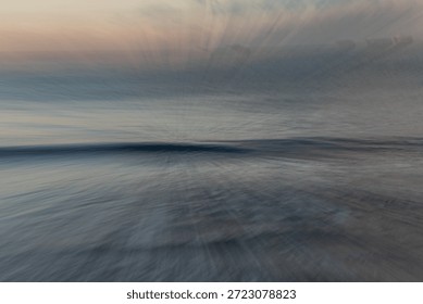 This image is a captivating example of Intentional Camera Movement (ICM) and long-exposure photography, capturing a coastal scene in a style that borders on abstract impressionism. The composition is defined by a central horizon line where a soft, dark wave crest provides a grounded focal point amidst an explosion of ethereal motion. The technique used appears to be a zoom burst or a radial pull, which creates a dynamic 