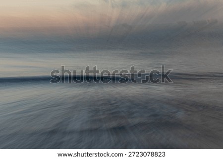 This image is a captivating example of Intentional Camera Movement (ICM) and long-exposure photography, capturing a coastal scene in a style that borders on abstract impressionism. The composition is defined by a central horizon line where a soft, dark wave crest provides a grounded focal point amidst an explosion of ethereal motion. The technique used appears to be a zoom burst or a radial pull, which creates a dynamic 