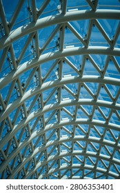 This image captures an abstract, low-angle view of the intricate glass and steel canopy forming the roof of the Bridge of Peace in Tbilisi, Georgia. The curving geometric framework creates striking patterns and reflections against a vibrant clear blue sky, highlighting modern architectural design.