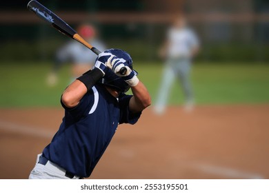 This image captures a baseball player in a batting stance, preparing to swing at an incoming pitch. The player wears a navy blue uniform, a helmet, and batting gloves, standing on a baseball field. - Powered by Shutterstock