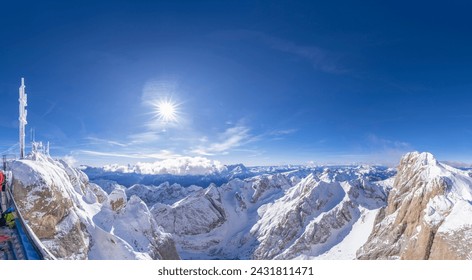 This image captures a breathtaking panoramic view of snow-covered mountain peaks under a bright blue sky in the Italian Alps. The radiant sun casts its light over the vast expanse of rugged mountains.