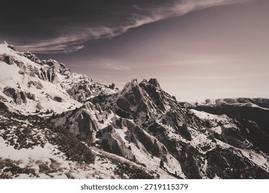 This image captures a breathtaking view of a snow-capped mountain range under a vibrant purple sky. The rugged peaks are covered in a blanket of snow, with patches of green trees visible among the snowy terrain. The sky transitions from deep purple at the horizon to lighter shades as it stretches upwards, creating a stunning contrast with the white snow. The scene conveys a sense of tranquility and natural beauty.