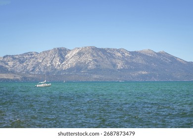 This image captures a calming scene of a small sailboat floating against the majestic mountains of Lake Tahoe