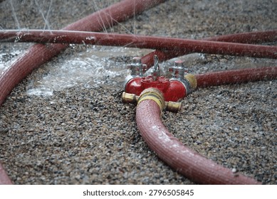 This image captures a close up of a red fire water hose connector or wye connection resting on a bed of gravel.