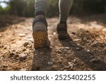 This image captures the close up view of a unknown man wearing hiking boots walking on a rocky and dirt path, emphasizing the rugged terrain and outdoor adventure