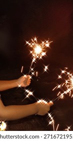 This image captures a close-up, vertical shot of a person’s arms and hands holding two lit sparklers against a dark, nocturnal background.
