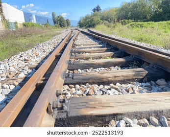 This image captures a close-up view of rustic railway tracks stretching into the distance, framed by a scenic countryside landscape. The weathered wooden sleepers and rusted steel rails evoke a sense  - Powered by Shutterstock