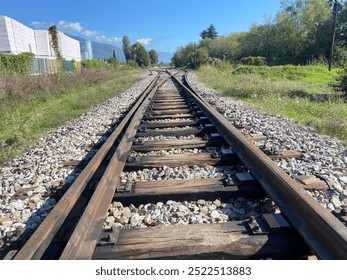 This image captures a close-up view of rustic railway tracks stretching into the distance, framed by a scenic countryside landscape. The weathered wooden sleepers and rusted steel rails evoke a sense  - Powered by Shutterstock