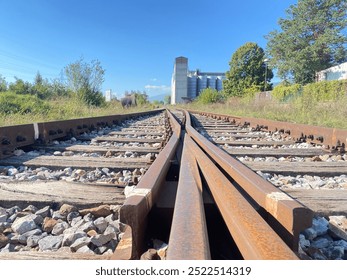 This image captures a close-up view of rustic railway tracks stretching into the distance, framed by a scenic countryside landscape. The weathered wooden sleepers and rusted steel rails evoke a sense  - Powered by Shutterstock