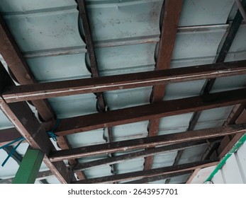 This image captures a close-up view of a traditional wooden roof frame with metal sheet covering. The wooden beams are arranged in a simple yet functional structure, showing signs of aging such as dis