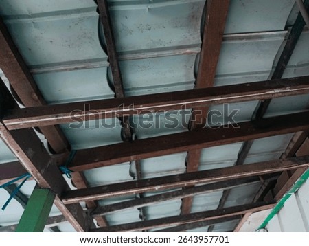 This image captures a close-up view of a traditional wooden roof frame with metal sheet covering. The wooden beams are arranged in a simple yet functional structure, showing signs of aging such as dis