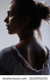 This image captures a contemplative young woman in profile, highlighting her delicate facial features and the subtle interplay of light and shadow.