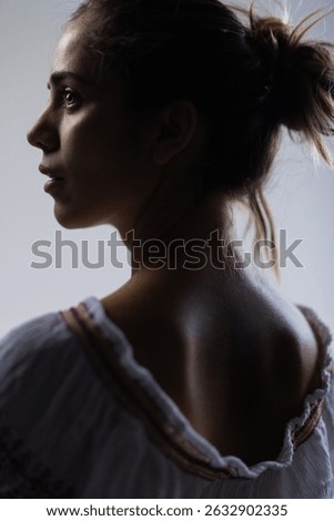 This image captures a contemplative young woman in profile, highlighting her delicate facial features and the subtle interplay of light and shadow.