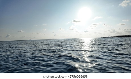 This image captures the dazzling reflection of the bright sun on the ocean's surface, extending towards the distant horizon under a clear blue sky.