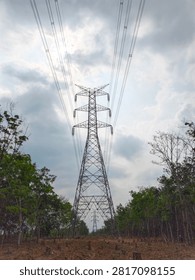 This image captures a dramatic view of a towering high-voltage power transmission tower set against a partially cleared landscape. The main tower, constructed of dark-colored metal latticework, dominates the frame, with power lines stretching upward and receding into the overcast sky. The tower’s intricate structure, with its wide base and tapered top, conveys a sense of strength and scale.
‎
‎On both main sides, there are rows of trees. On the left, the trees appear lush and green, with dense foliage. On the right, the trees are sparser, some of which look bare and dry, suggesting logging or less-than-ideal environmental conditions. The area in front of the tower looks like excavated or cleared land, with tree stumps scattered across the reddish-brown surface.
‎
‎The sky above is covered by thick gray clouds, creating a somewhat gloomy yet majestic atmosphere. Sunlight struggles to break through the gaps in the clouds, casting a faint glint on the power lines. In the distance, another similar transmission tower is visible, indicating that this is part of a vast power grid.
‎
‎Overall, this image blends industrial and natural elements. The contrast between the sturdy man-made structure and the surrounding vegetation, along with the dramatic sky, creates an intriguing visual composition. This image can be interpreted as.