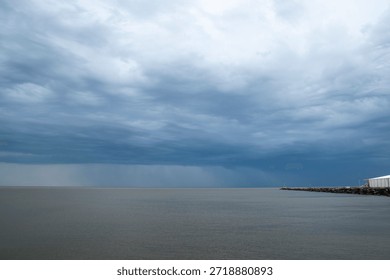 This image captures a dramatic weather event, specifically the approach of a significant storm over the estuary of the Rio de la Plata in Uruguay. The scene is dominated by heavy, dark cumulonimbus clouds, often referred to as thunderstorm clouds, which form tall towers as air rises rapidly.