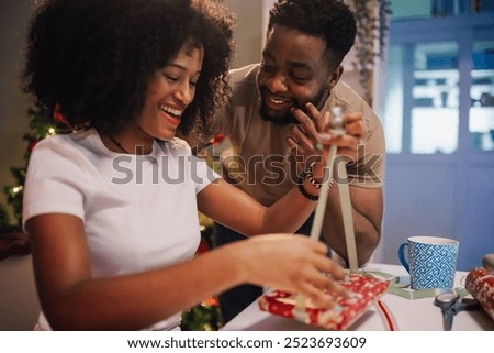 This image captures a dynamic duo's joy as they engross themselves in gift wrapping, complemented by a festive atmosphere complete with seasonal decorations.