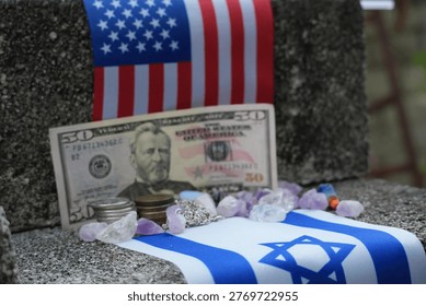 This image captures the flags of the USA and Israel, juxtaposed with a prominent fifty-dollar bill, a stack of coins, and various amethyst crystals. It symbolizes the blend of political alliance, economic factors, and spiritual undercurrents.
