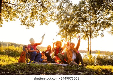 This image captures a heartwarming scene of a multi-generational family enjoying a picnic by a tranquil lakeside during the golden hour. The sun sets, casting a warm, golden light that enhances the - Powered by Shutterstock