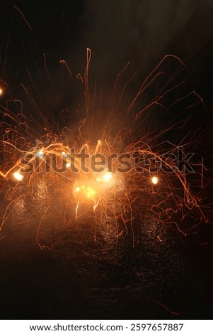 This image captures an intense firework explosion with bright orange and yellow sparks against a dark background. The long exposure effect creates light trails, giving a sense of motion and energy.