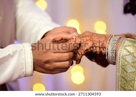 This image captures an intimate moment during a traditional Indian wedding or engagement ceremony, specifically the exchange of rings.