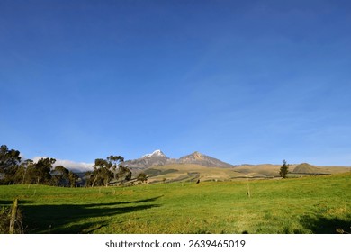 This image captures the majesty of the North and South Ilinizas volcanoes at sunrise, seen from the green fields of El Chaupi, Ecuador. 