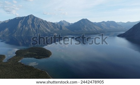 This image captures a serene landscape in Yukon, Canada where majestic mountains are reflected in the calm waters of a vast lake, showcasing the harmonious interplay of natural elements.