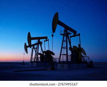 This image captures a serene twilight moment in a desert landscape where oil pumps are actively extracting crude oil. The pumps, silhouetted against the vibrant evening sky, highlight the intersection of industrial activity and natural environment. The scene underscores the importance of energy production and its impact on the landscape.