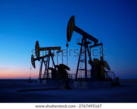 This image captures a serene twilight moment in a desert landscape where oil pumps are actively extracting crude oil. The pumps, silhouetted against the vibrant evening sky, highlight the intersection of industrial activity and natural environment. The scene underscores the importance of energy production and its impact on the landscape.
