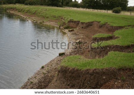 This image captures significant soil erosion along a lake bank revealing multiple layers of earth and green grass. The environmental degradation highlights the impact of natural forces.