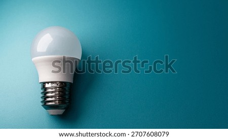 This image captures a single, energy-saving LED light source, emphasizing its compact shape against a complementary blue background with significant room for text overlay.