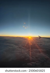This image captures a stunning view from an airplane window during sunset. The airplane wing is visible on the right side of the frame, with the setting sun casting golden rays across the horizon.