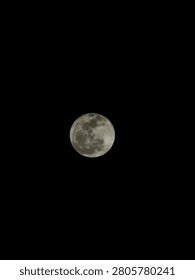 This image captures a stunning view of the full moon shining brightly against a clear, pitch-black night sky. Positioned near the center of the frame, the moon appears highly detailed, with its craters, dark lunar maria, and textured surface clearly visible. The simplicity of the composition draws all attention to the moon, creating a sense of serenity and wonder. The strong contrast between the bright lunar surface and the dark sky enhances the image's clarity, making it an elegant and captivating photograph of the night sky.