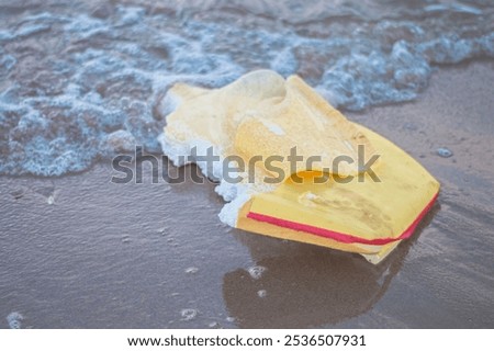 This image captures a surfboard left on the beach after a challenging wave session. With a visible crack, glued sand, and a weathered look, the board reflects the resilient and adventurous spirit