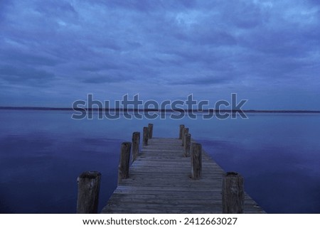 This image captures a tranquil scene at dusk or dawn, with the focus on a wooden dock that extends into the water.