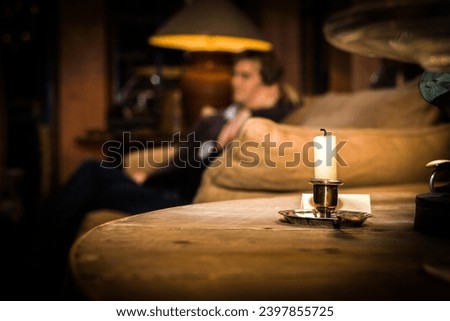 This image captures the tranquility of an evening spent in contemplation, with a single lit candle in the foreground providing a warm, focused light that contrasts with the dimly lit, cozy interior