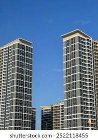 This image captures two high-rise apartment buildings with modern design under a clear blue sky. The buildings are gray and yellow, with many windows and balconies.