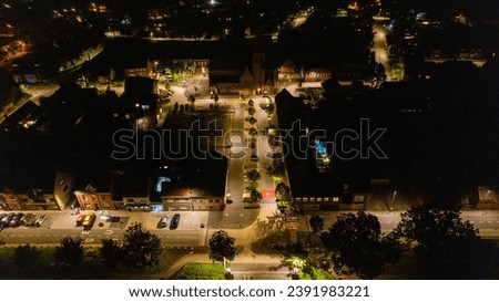 This image captures the vibrant life of an urban street at night, viewed from above. Streetlights cast a warm, inviting glow, illuminating paths and thoroughfares. The arrangement of the lights