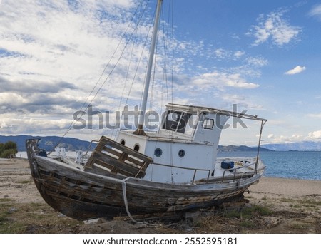 This image captures a weathered boat resting on a sandy shore, creating a poignant scene of abandonment. The boat, with its rustic wooden structure, showcases signs of wear and age, with peeling paint