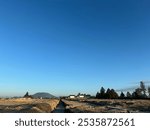 This image captures a wide-open landscape under a clear blue sky. The scene is mostly barren, with dry soil and a trench running down the middle, possibly for construction or drainage purposes.