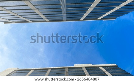 This image captures a worm's-eye view of modern buildings with glass facades against a clear blue sky, emphasizing urban architecture and open space