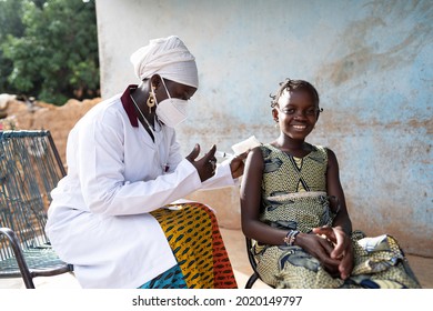 In This Image, A Courageous Little African Girl Is Smiling Into The Camera While Receiving A Vaccine Shot By A Gentle Young Black Nurse Sitting Next To Her On A Rural Hospital Veranda