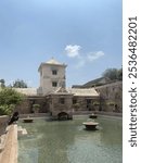 This image depicts an ancient building that has a central courtyard. In the center of the courtyard is a magnificent water feature, such as a still pool with several decorative fountains.