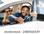 This image depicts a happy couple receiving the keys to their new car from a dealership representative. The man is sitting in the drivers seat of a white sedan and is reaching out to take the keys