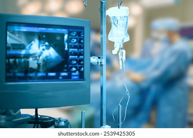 This image depicts a hospital or surgical setting, with a medical monitor displaying diagnostic imaging, possibly an ultrasound or X-ray, and an intravenous (IV) fluid bag in the foreground.  - Powered by Shutterstock