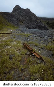 This Image Depicts An Old Rusty Car Part Pointing Towards A Large Mountain. The Foreground Has A Warm Lighting Cast Upon It, But The Mountain Has Cold Lighting That Further Dramatizes Its Size.