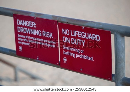 This image displays a red warning sign near the beach, emphasizing water safety hazards. 