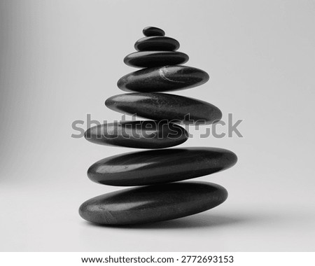 This image features a carefully arranged stack of smooth black stones on a plain gray background. The stones are balanced in a tower-like structure, evoking a sense of calm and serenity. The simple yet elegant composition makes it perfect for use in wellness, meditation, and relaxation contexts.